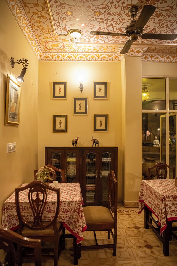Un comedor con ventilador de techo, cuadros enmarcados y un mueble con puertas de cristal.