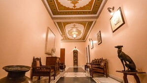 A hallway with ornate ceiling, framed artwork, and a statue of a dog.