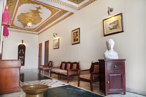 Un hall d’entrée spacieux doté d’un sol en marbre, de bancs en bois, d’un buste sculpté et d’œuvres d’art encadrées qui ornent les murs.