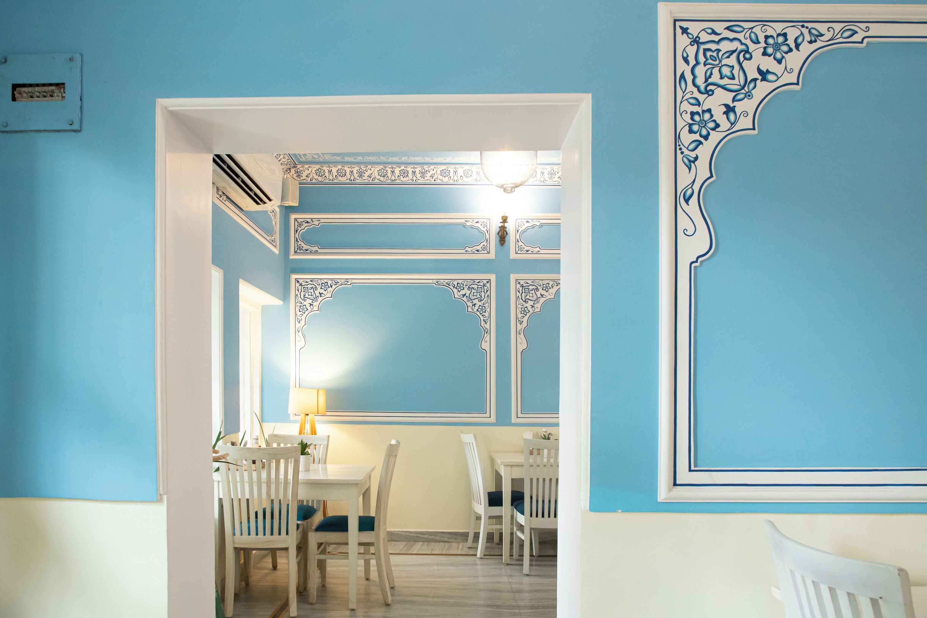 A dining area with a blue and white color scheme, featuring a table and chairs, a lamp, and decorative wall moldings.