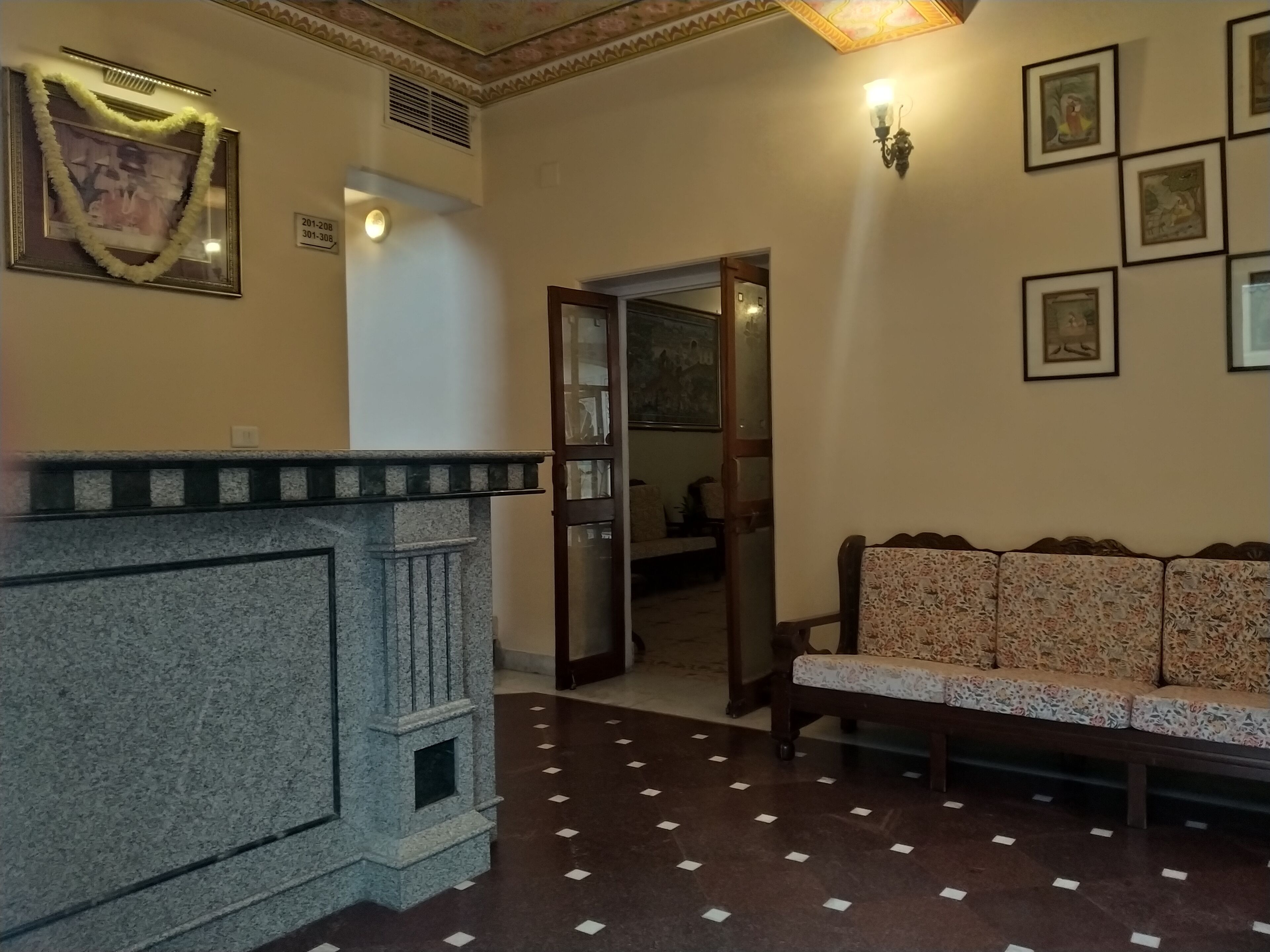 A lobby with a reception desk, a sofa, a wall with framed pictures, and a door leading to another room.
