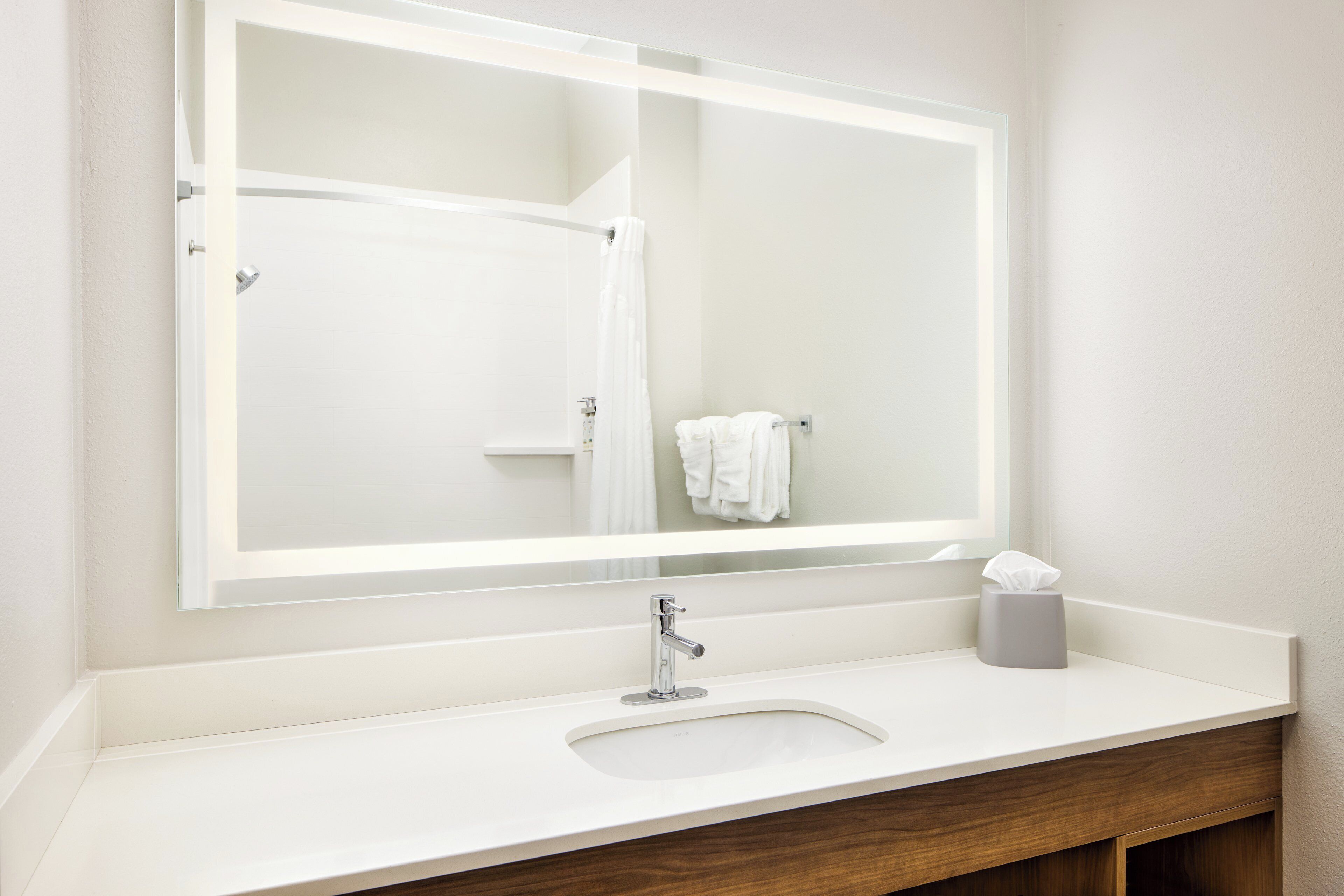 A bathroom with a large mirror, a sink, and a towel rack.