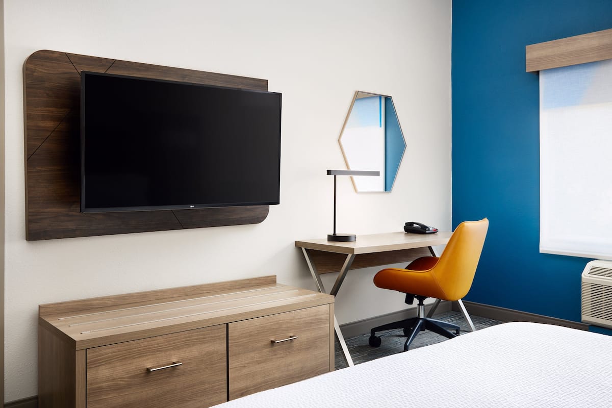 A modern hotel room with a large flat-screen TV, a desk with a chair, and a bed.
