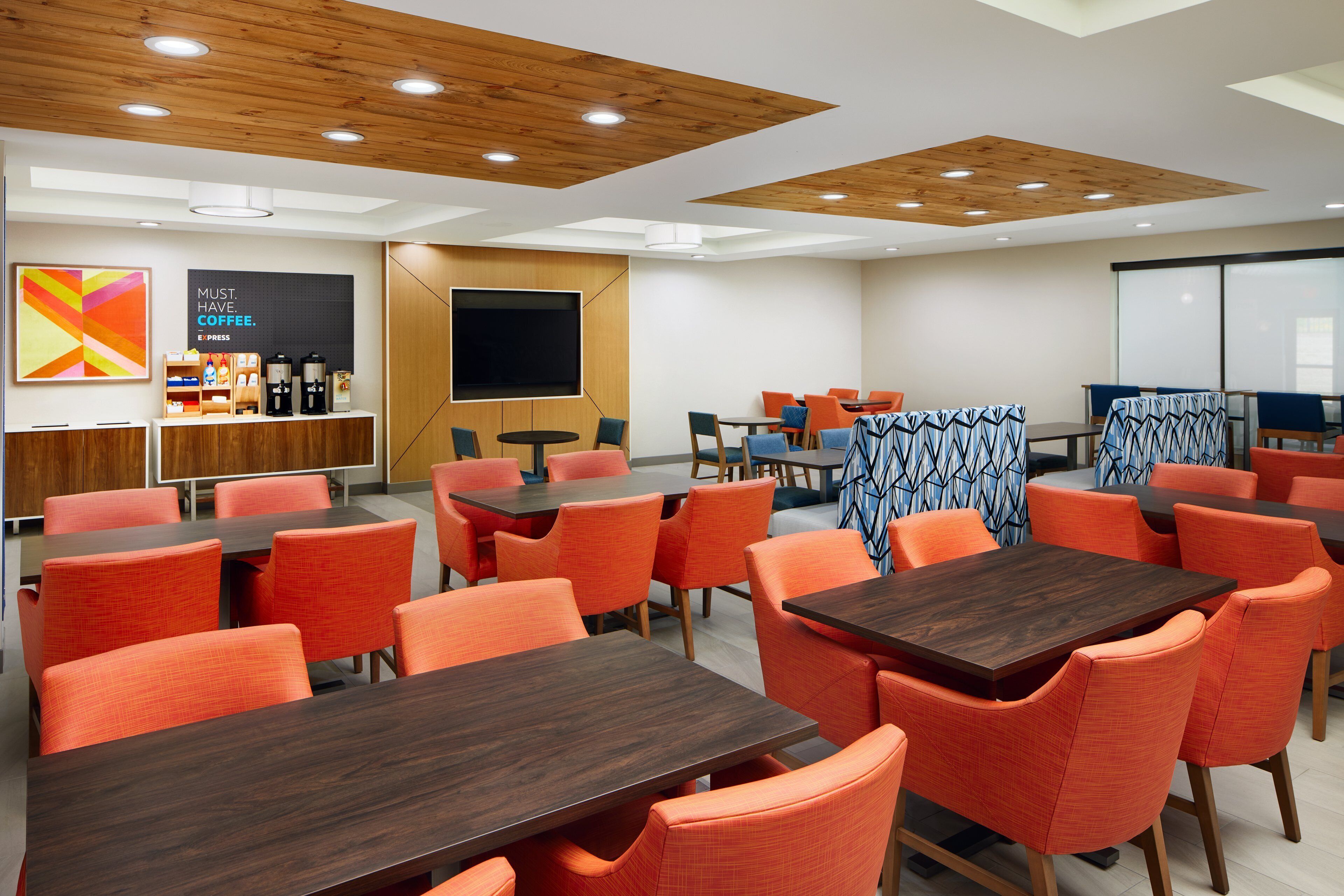 Un salón de conferencias moderno con paneles de techo de madera, sillas anaranjadas y una pantalla grande.