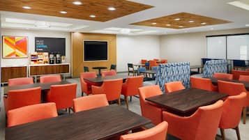 Un salón de conferencias moderno con paneles de techo de madera, sillas anaranjadas y una pantalla grande.