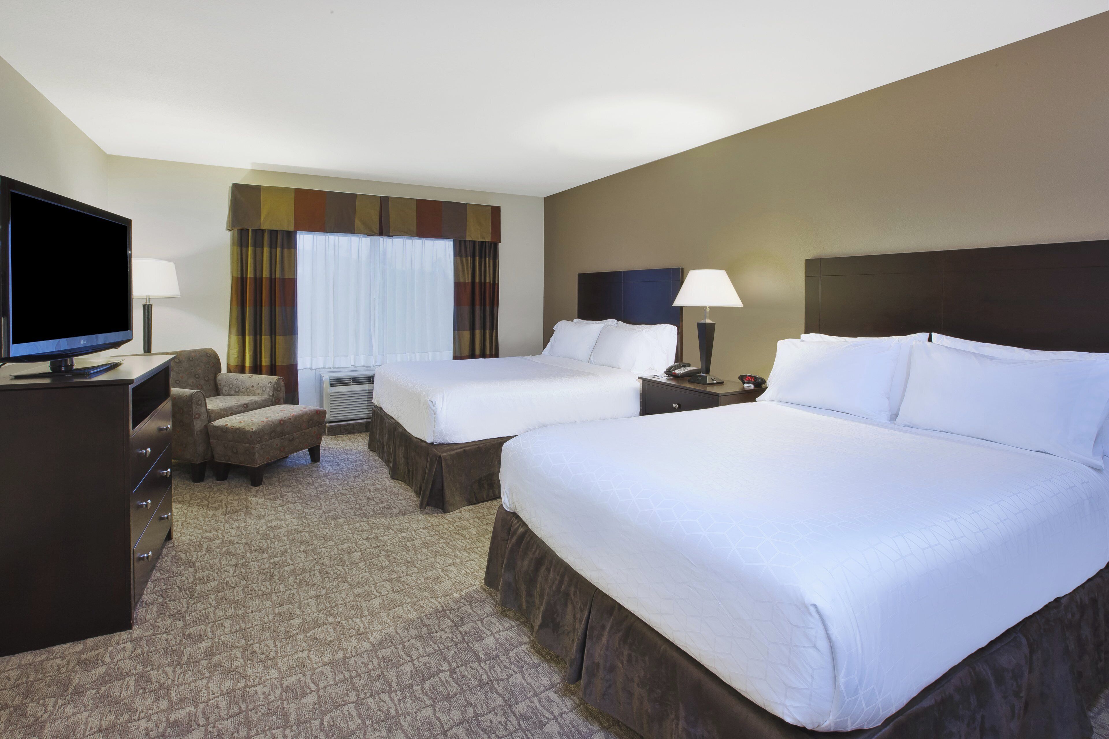 Quarto de hotel com duas camas, televisão, escrivaninha e uma cadeira.