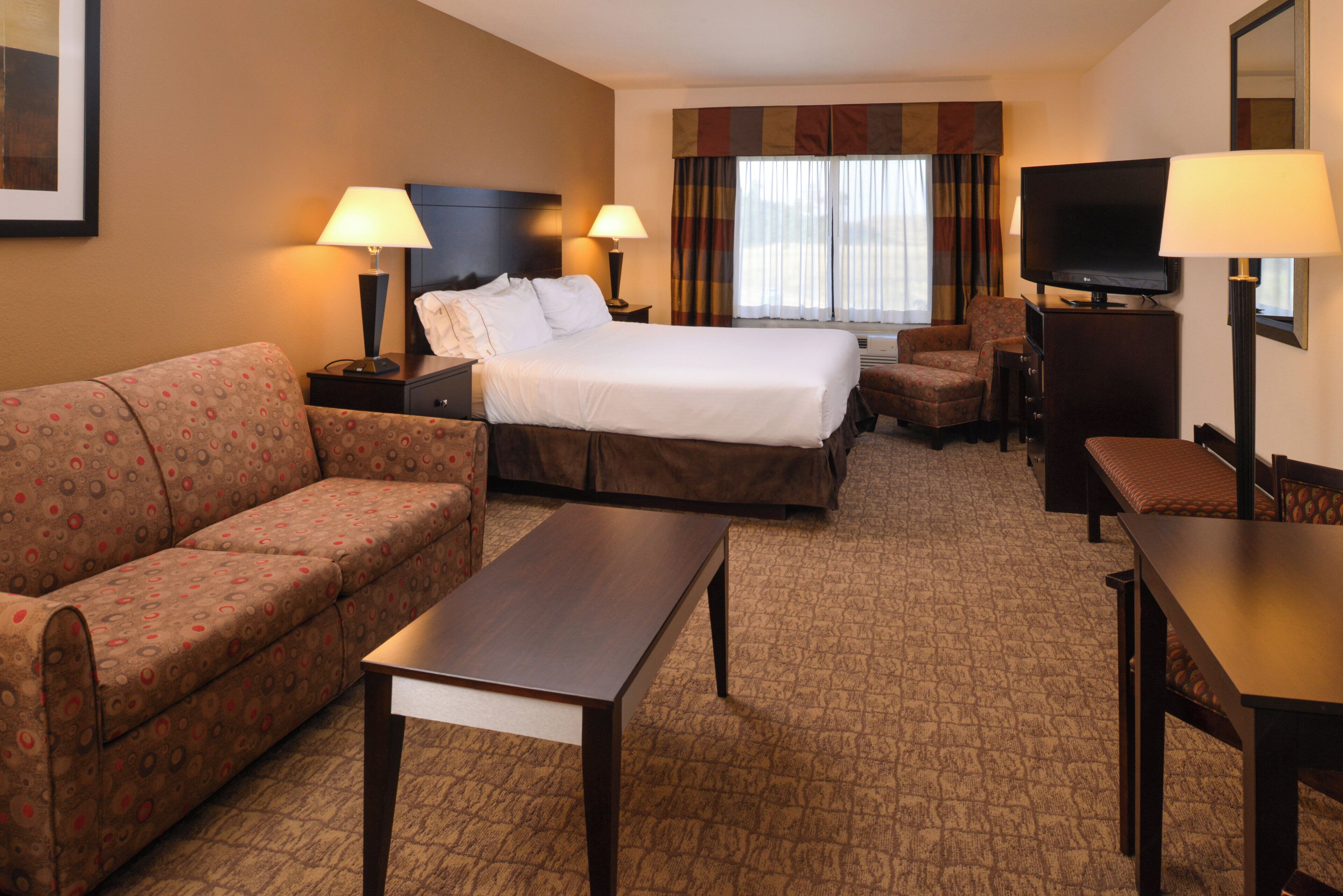 A hotel room with a bed, a sofa, a desk, a chair, and a television.