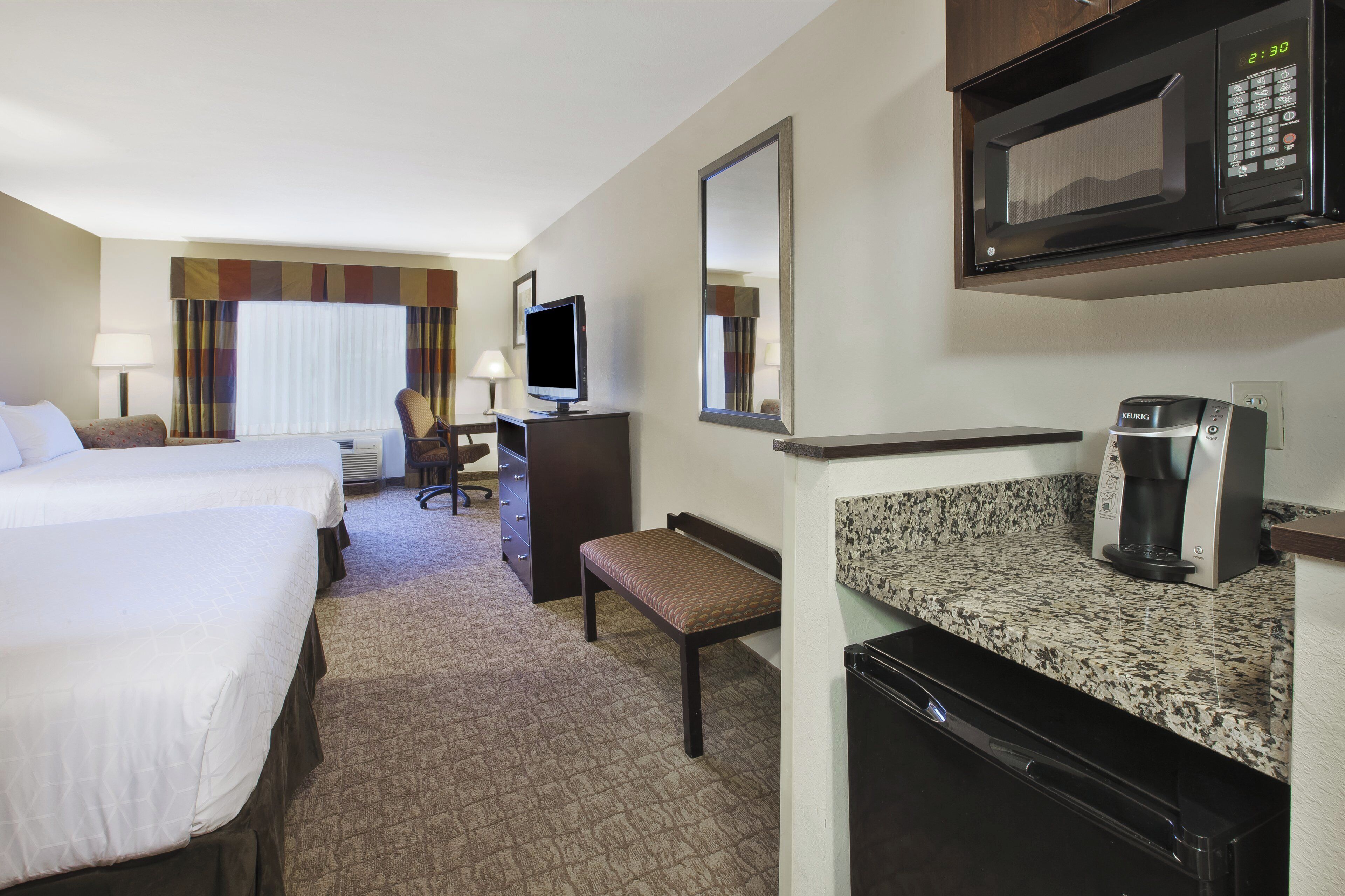 A hotel room with two beds, a desk with a television, a coffee maker, and a microwave.
