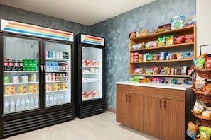 Una tienda de conveniencia con dispensadores de bebidas frías, estantes con snacks y una variedad de productos envasados.