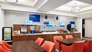 Un bar à petit-déjeuner moderne offrant un large choix d’aliments, notamment des produits de boulangerie, des céréales et des plats chauds. On peut voir des chaises oranges et une table en bois au premier plan.