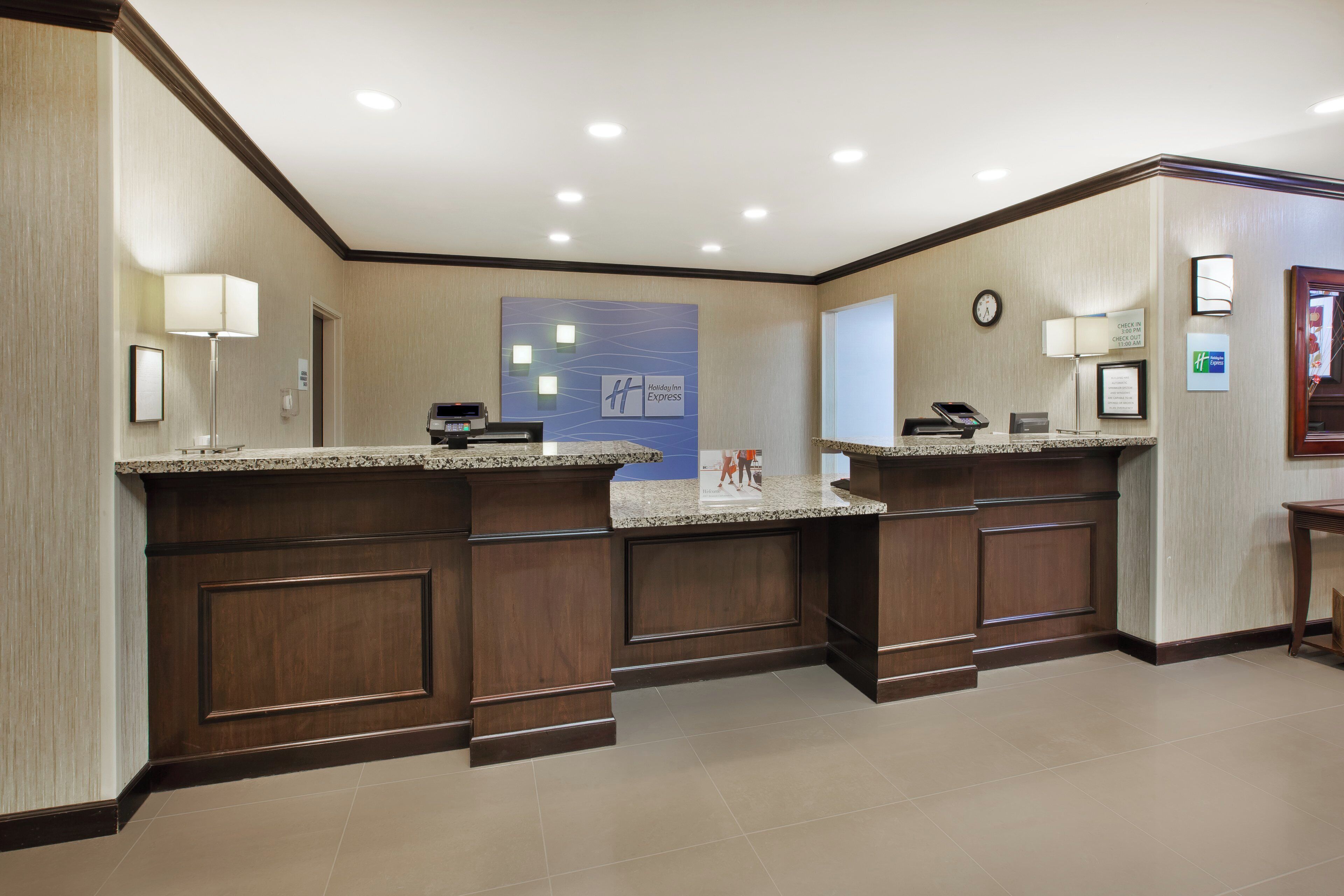 A hotel reception area with a check-in counter, a clock, and a Holiday Inn Express sign.