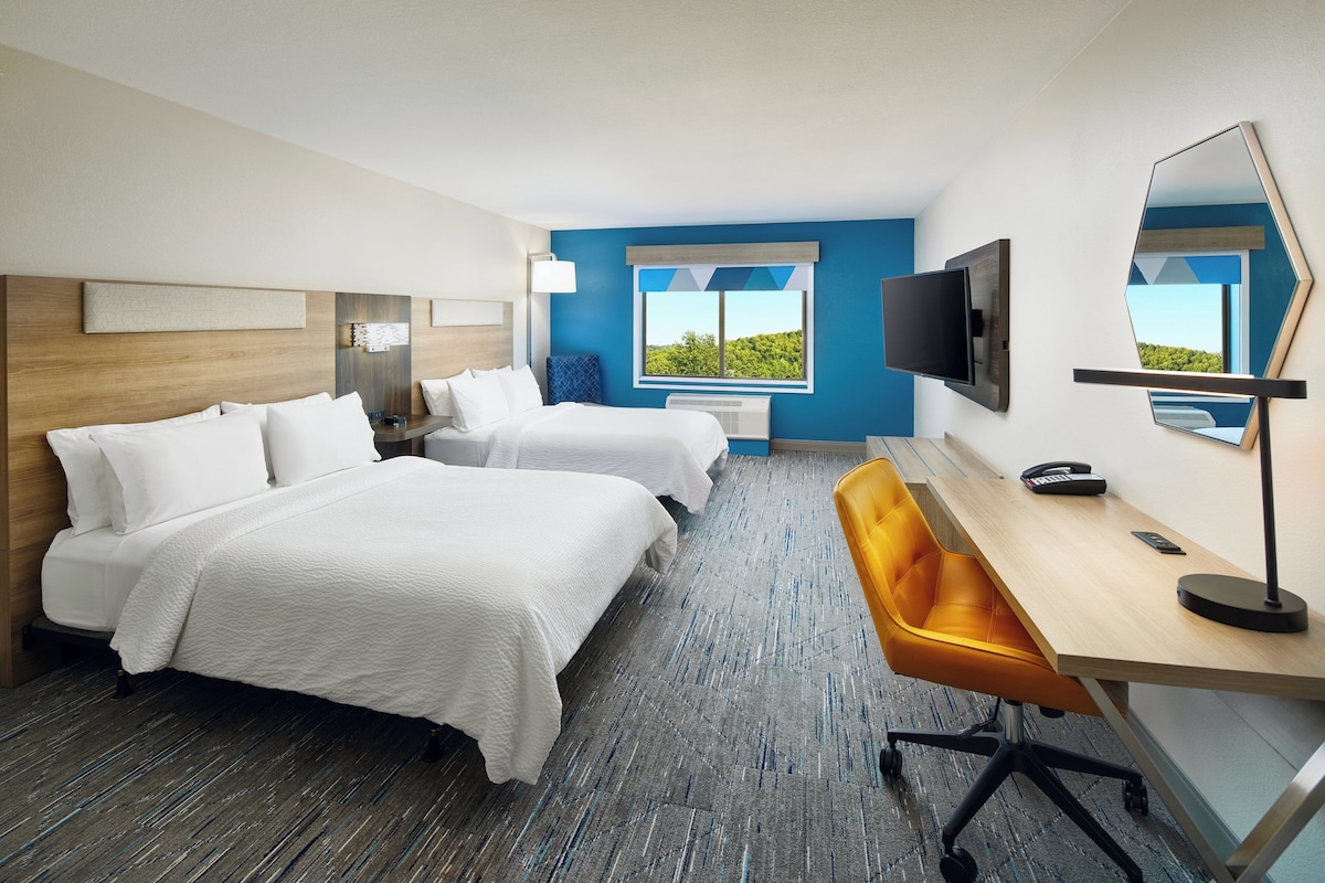 Habitación de hotel con dos camas, un escritorio, una silla, un televisor y una ventana con vistas a zonas verdes.