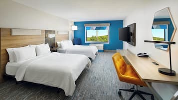 A hotel room with two beds, a desk, a chair, a TV, and a window with a view of greenery.