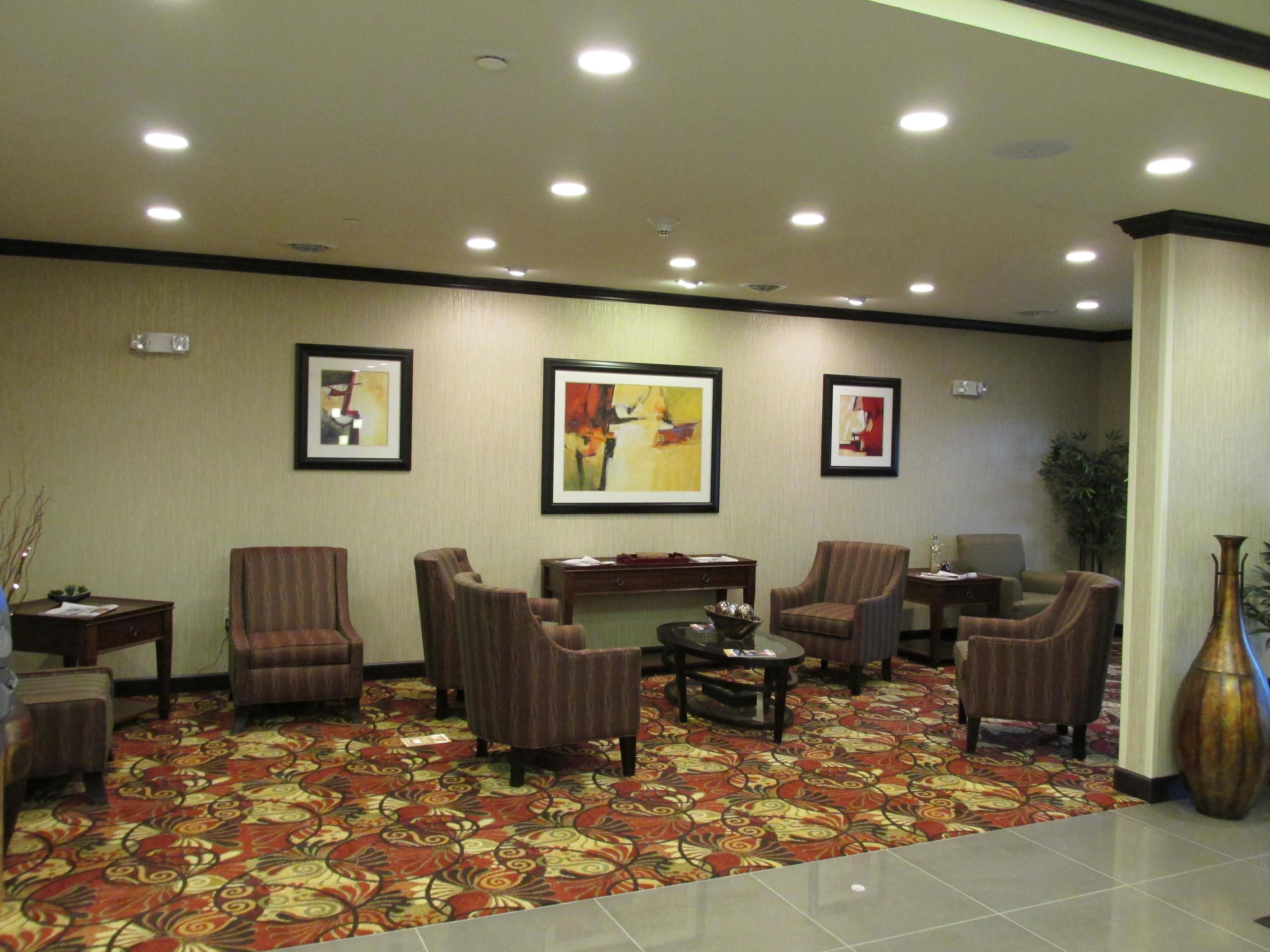A lobby with patterned carpet, several armchairs, a coffee table, framed artwork on the walls, and a large vase.