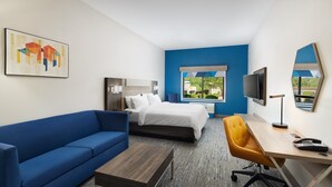Une chambre d’hôtel avec un lit, un canapé bleu, un bureau avec une chaise et un téléviseur.