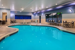 Una piscina interior con indicador de profundidad de 1,5 metros, rodeada de sillones de descanso y mesas, y vistas al exterior a través de amplios ventanales.