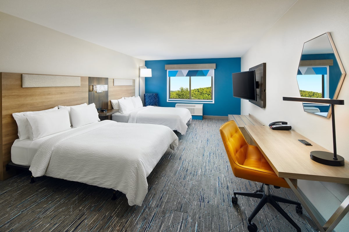 A hotel room with two beds, a desk, a chair, a TV, and a large window with a view.