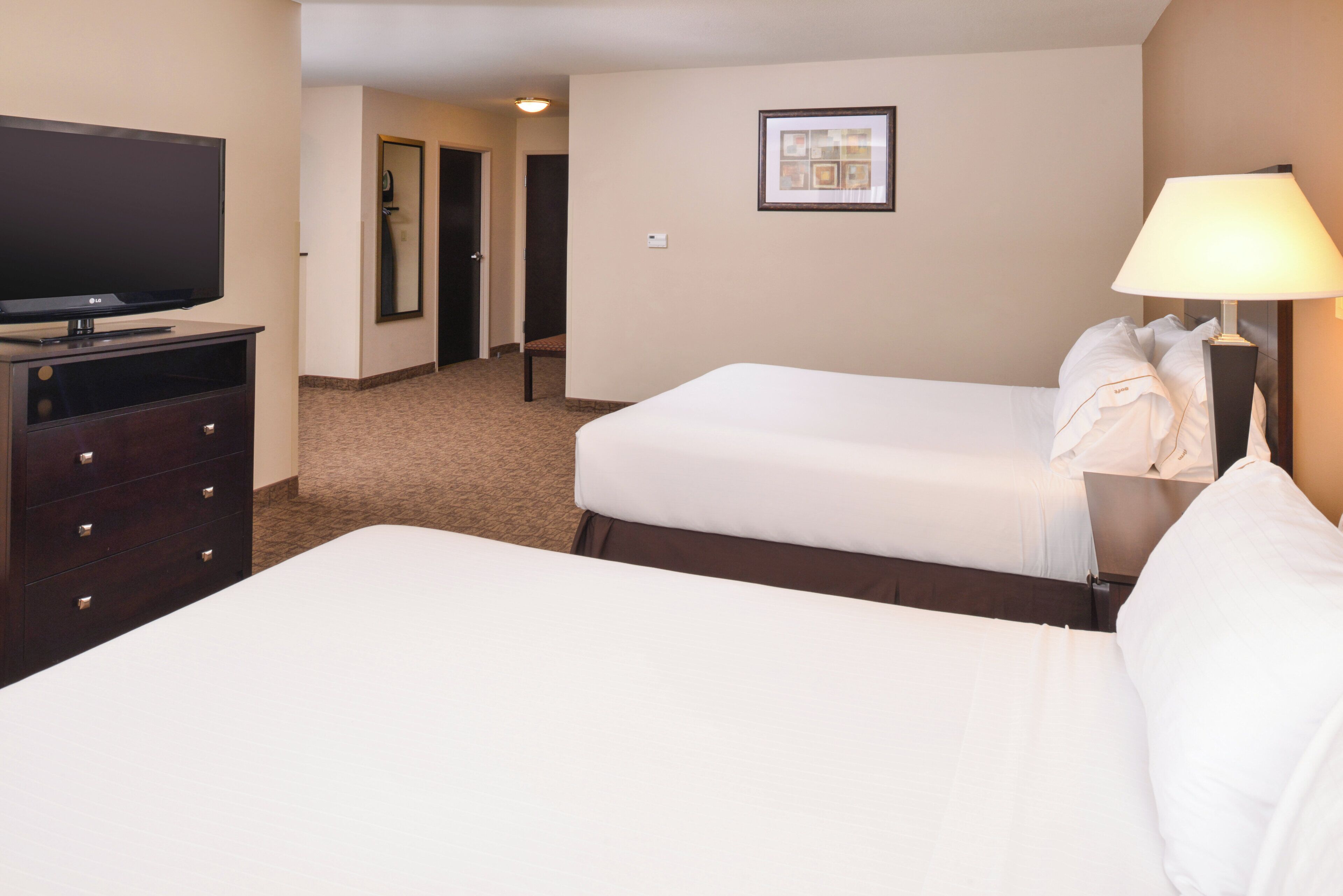 A hotel room with two beds, a TV, a dresser, and a lamp.