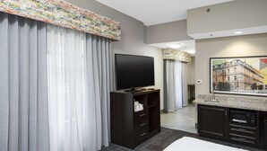 A hotel room with a large flat-screen TV, dark wooden furniture, a kitchen area with a microwave, and a painting on the wall. - Hampton Inn & Suites Raleigh Downtown (Raleigh)
