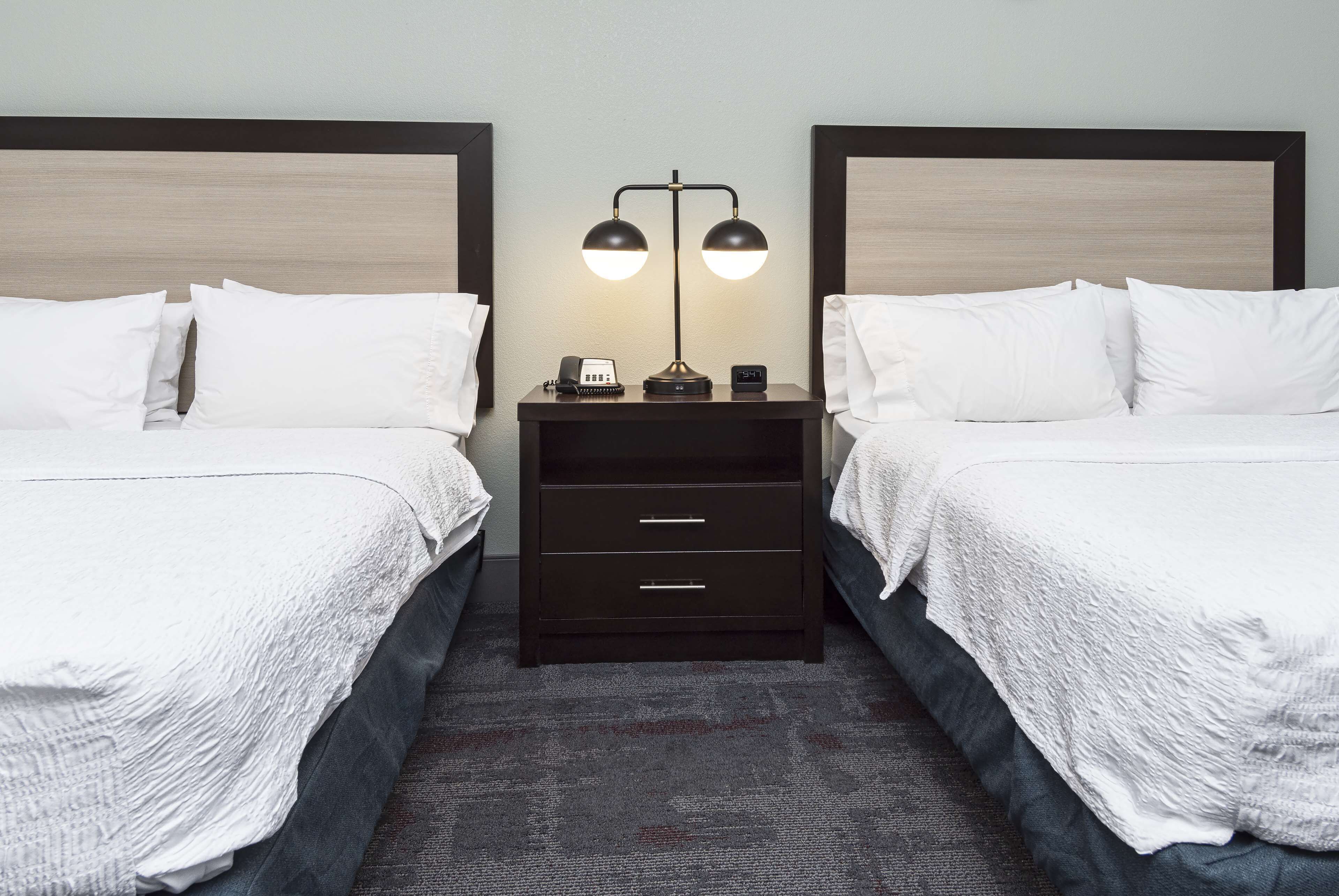 A hotel room with two single beds, a nightstand with a lamp, a phone, and a clock.
