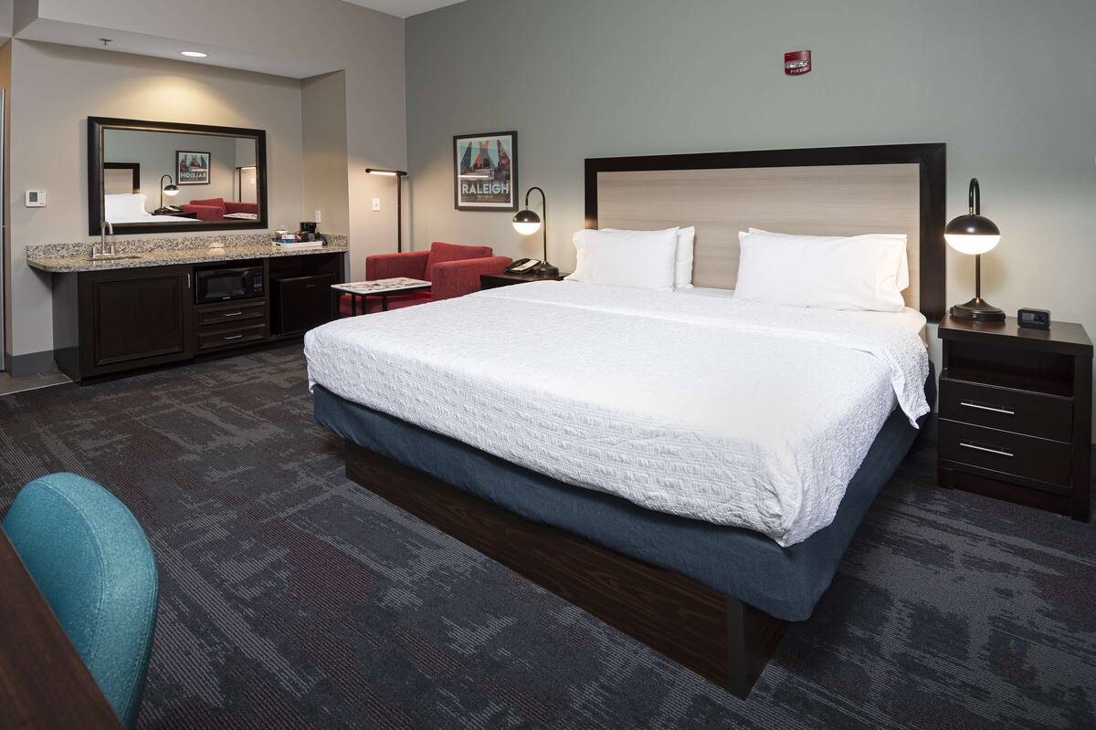 A hotel room with a large bed, a desk with a chair, a microwave, a coffee maker, and a framed picture on the wall.
