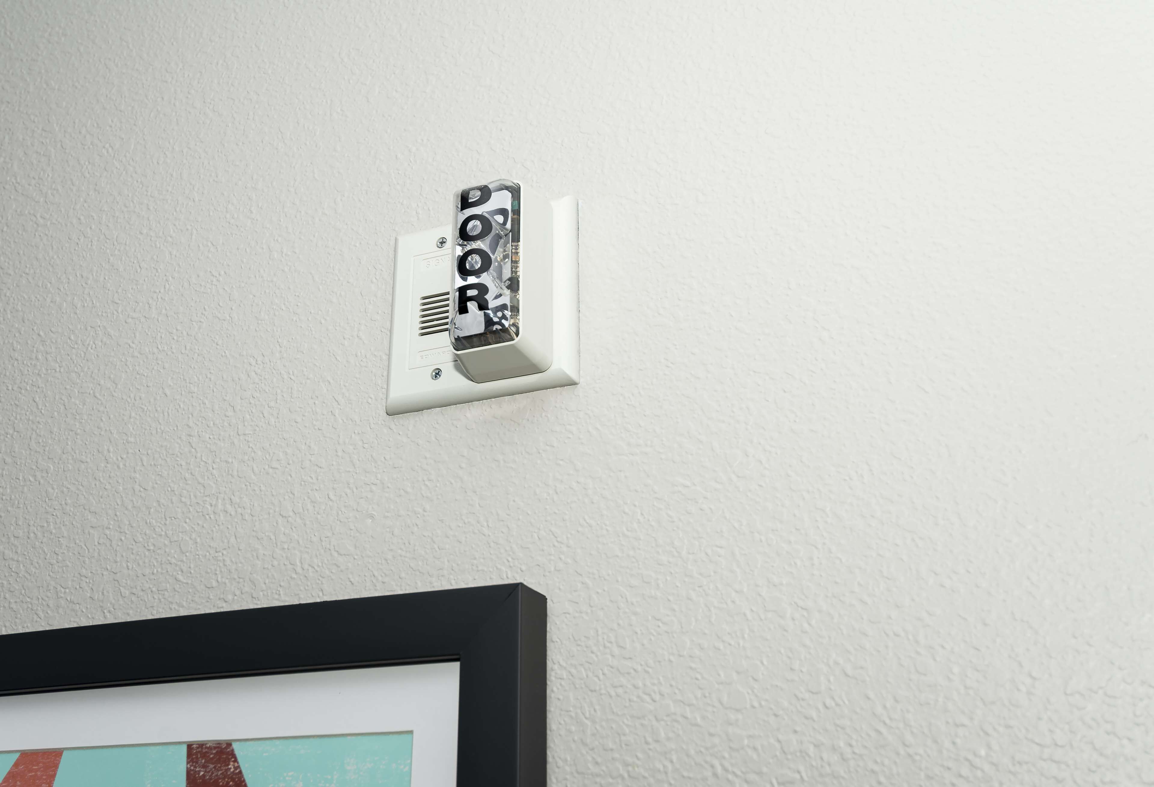 A doorbell with a "DOOR" sign on a white wall.
