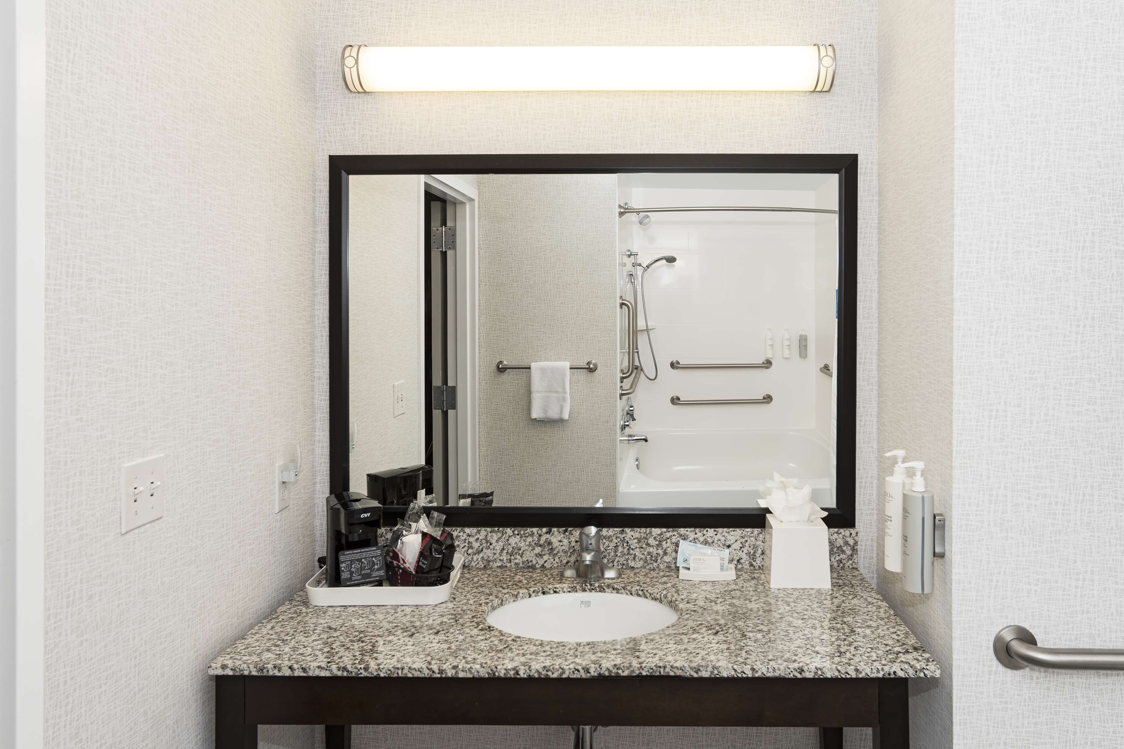 A bathroom with a granite countertop, a white sink, a large mirror, and a shower area visible through the door.