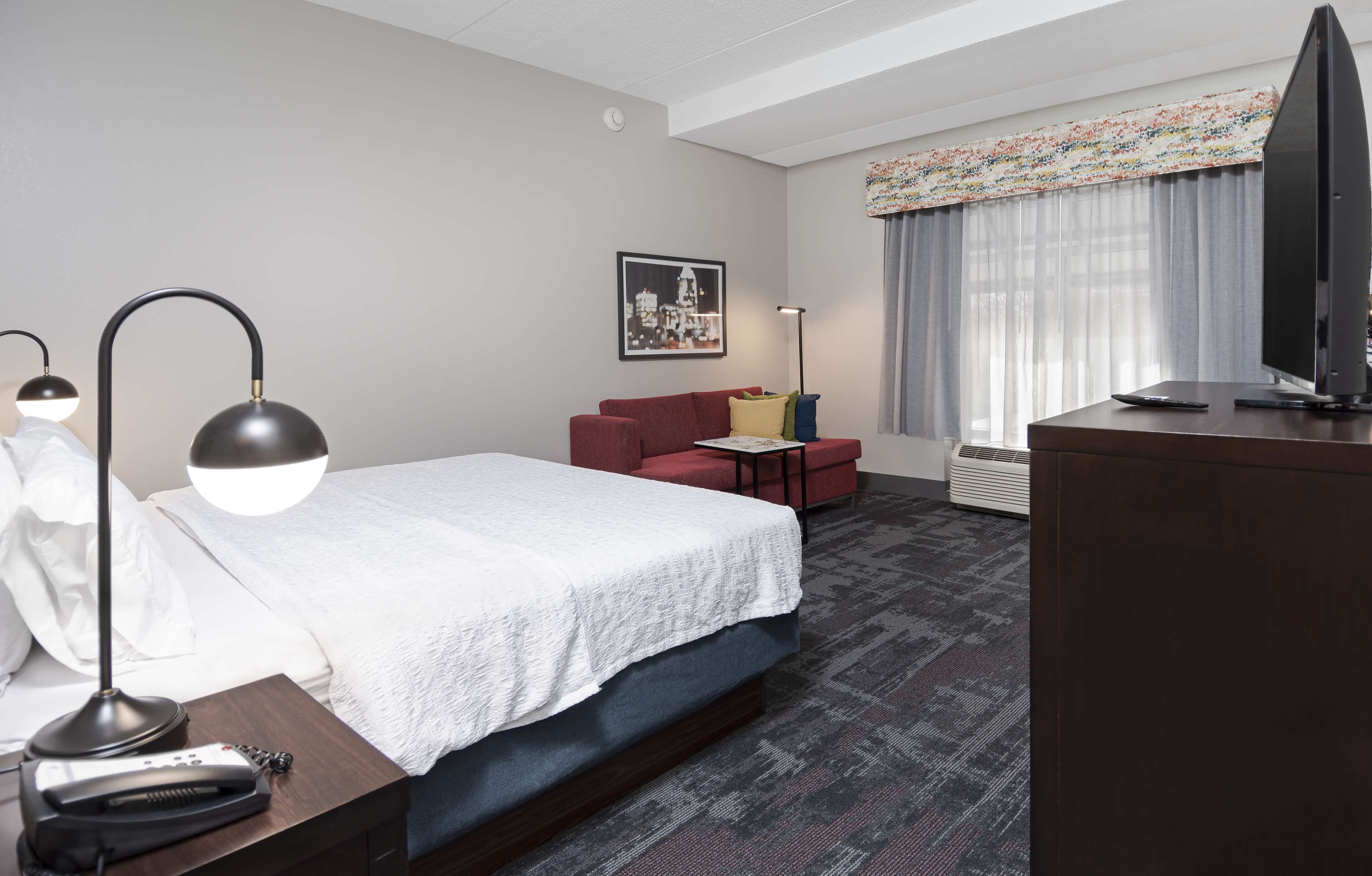 Una habitación de hotel con una cama, un escritorio, una silla, un televisor y una ventana con cortinas.