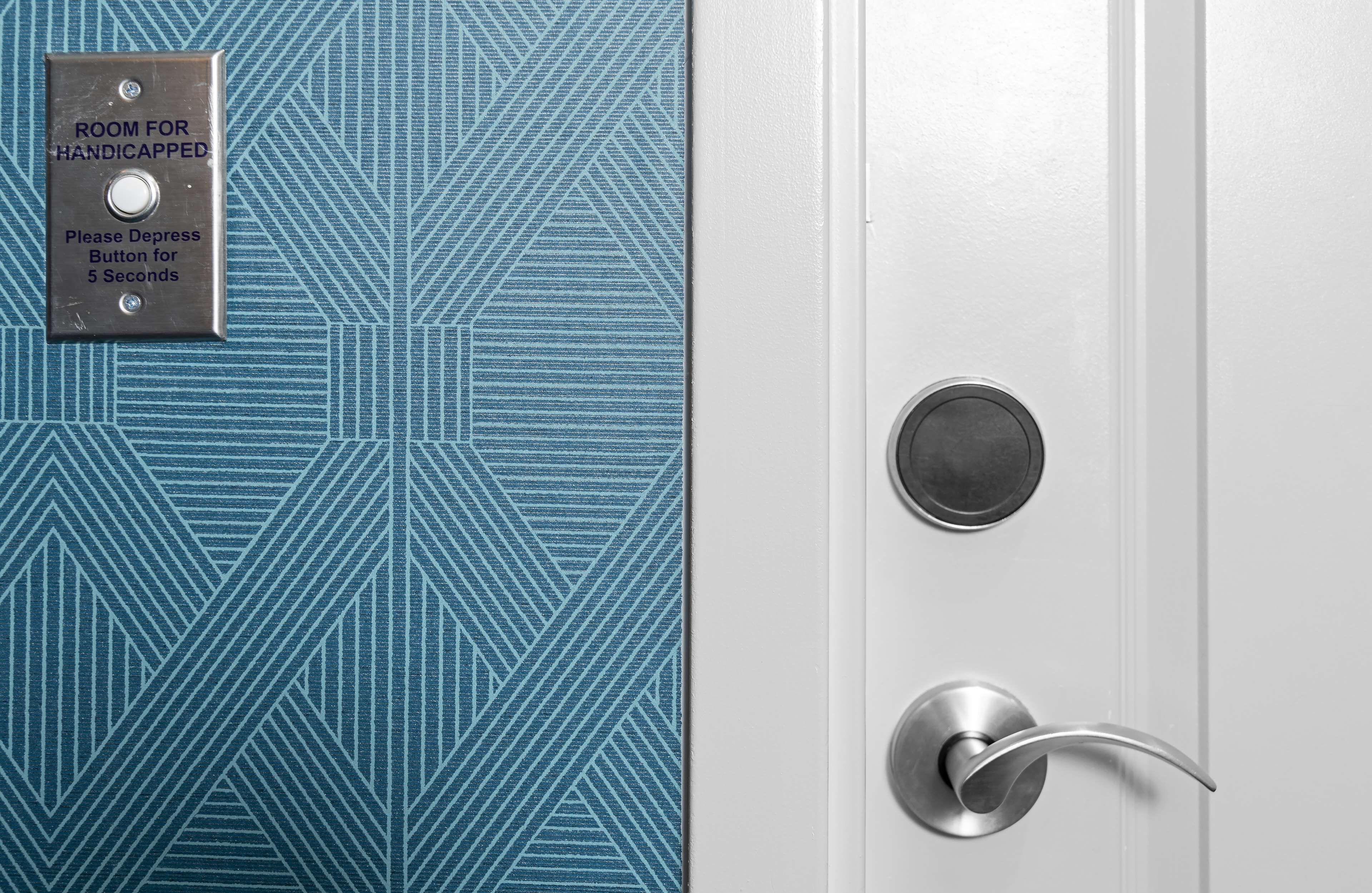 Une porte donnant sur un mur à motifs bleus et une pancarte indiquant une pièce réservée aux personnes handicapées.