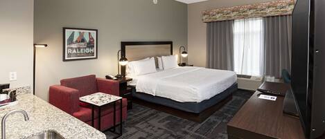 A hotel room with a bed, a desk, a chair, a small table, a sink, and a television.