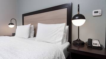 A hotel room with a large bed, two bedside lamps, a bedside phone, and a thermostat on the wall.
