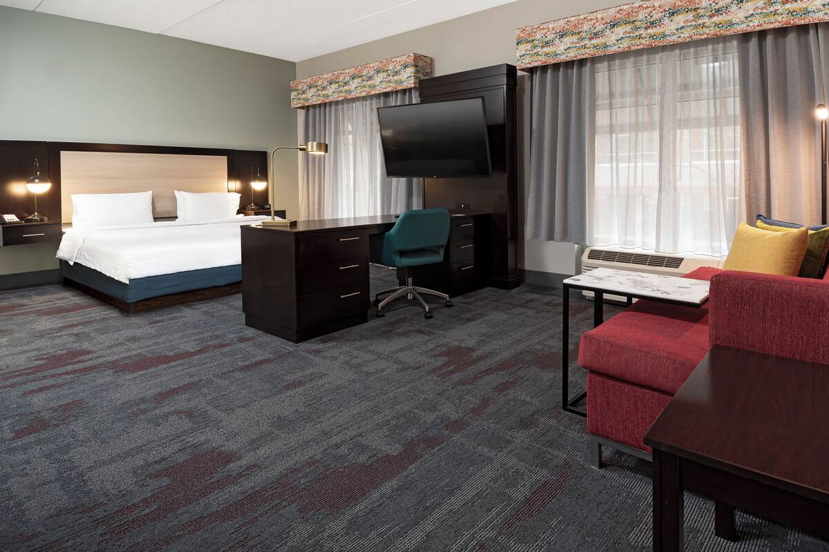 A hotel room with a bed, a desk, a chair, a TV, and a desk lamp.