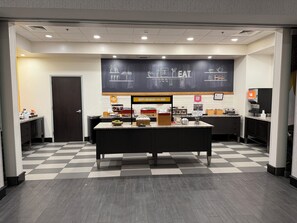 A breakfast area with a checkered floor, a central counter with food items, and a wall with food-related illustrations and text.