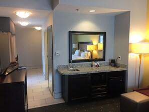 A hotel bathroom with a large mirror, a sink with a granite countertop, a dark vanity, and a toilet.