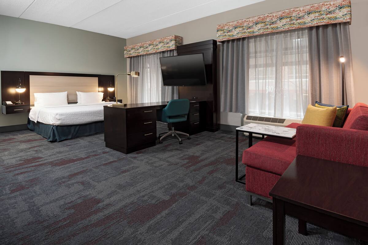 A hotel room with a bed, desk, chair, TV, and a red sofa.