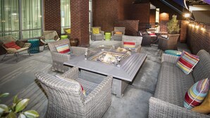 An outdoor seating area with wicker furniture, a central fire pit, and brick walls. - Hampton Inn & Suites Raleigh Downtown (Raleigh)