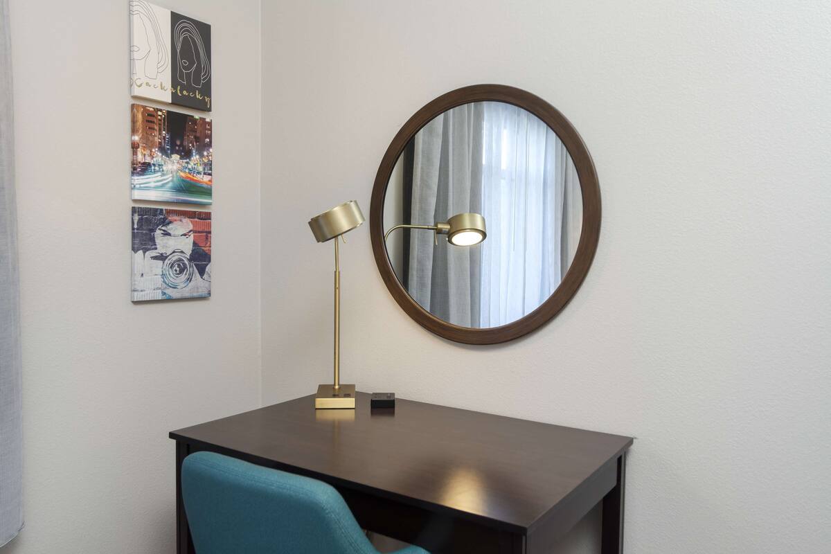 A desk with a round mirror, a lamp, and three framed artworks on the wall.