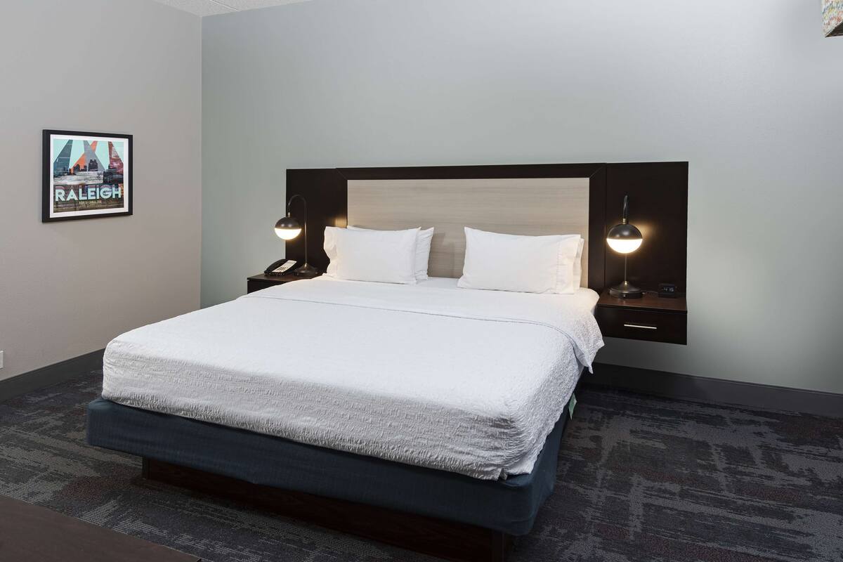 A neatly made bed with white linens, a dark headboard, and two bedside tables with lamps.