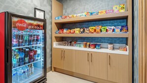 A vending machine with a Coca-Cola sign, shelves stocked with snacks and drinks, and a wooden cabinet with various food items.