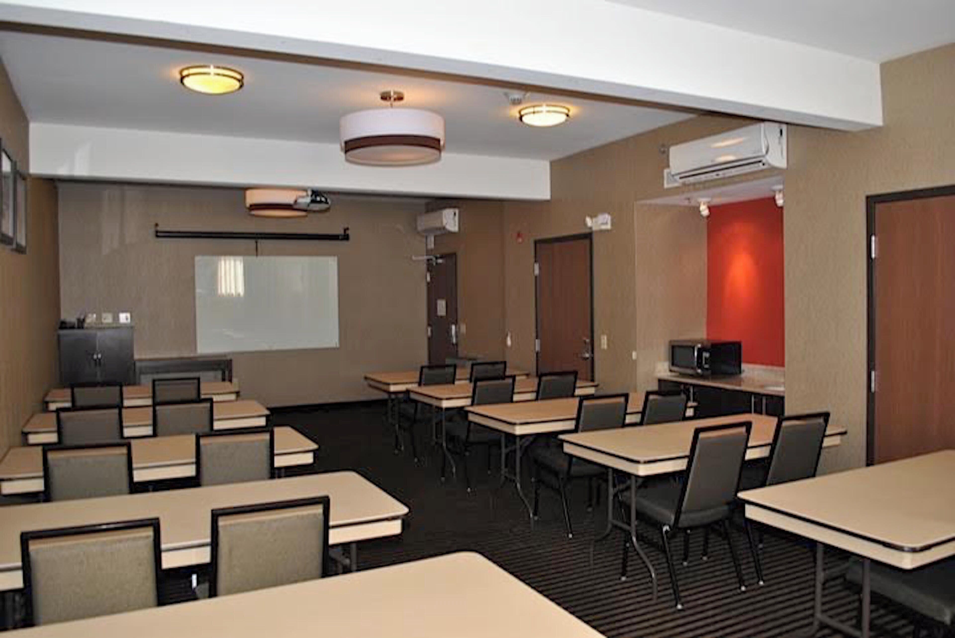 A conference room with tables, chairs, a projector screen, and an air conditioning unit.