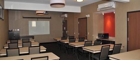 A conference room with tables, chairs, a projector screen, and an air conditioning unit.