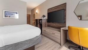 A modern hotel room with a large bed, a flat-screen TV mounted on the wall, a wooden cabinet, a yellow chair, and a small desk. - Holiday Inn Express Pittsburgh East - Mall Area by IHG (Homestead)