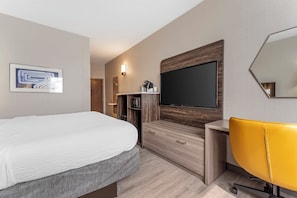 A modern hotel room with a large bed, a flat-screen TV mounted on the wall, a wooden cabinet, a yellow chair, and a small desk. - Holiday Inn Express Pittsburgh East - Mall Area by IHG (Homestead)