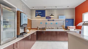 Un moderno comedor con un mostrador de autoservicio, un refrigerador con bebidas y una pared con indicaciones.