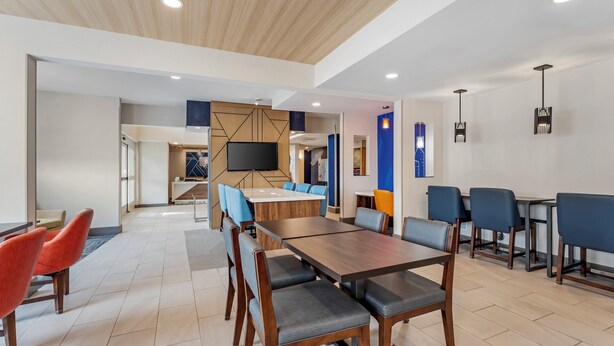 A modern dining area with wooden tables and chairs, a flat-screen TV, and pendant lights.
