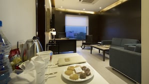 Una habitación de hotel moderna con comedor, sofá, mesa de centro y vistas de la ciudad a través de la ventana.