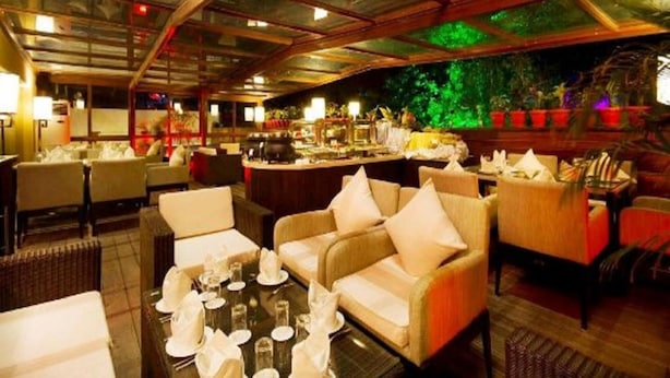 Un restaurante con techo alto, paneles de vidrio y una pared verde. Las mesas están preparadas con manteles blancos y sillas.