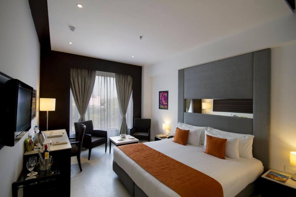 A hotel room with a bed, a desk, a chair, a TV, and a window with curtains.