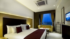 Una habitación de hotel con una cama grande, un sofá, un televisor y un ventanal con cortinas.