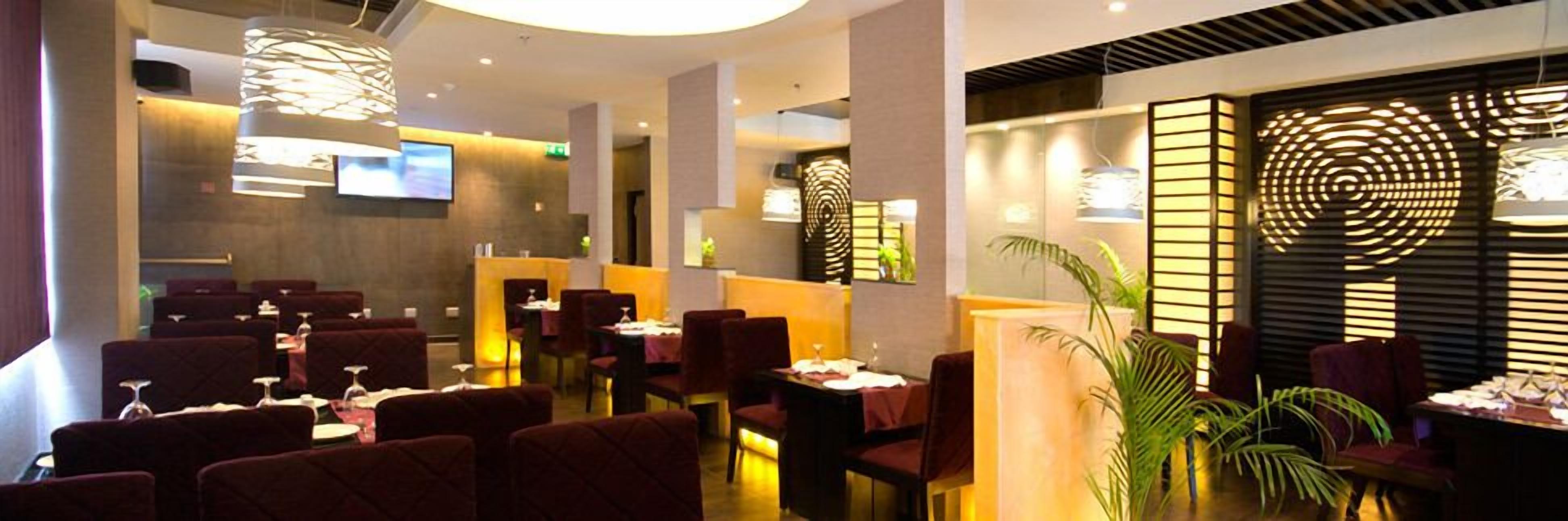 Ein modernes Restaurantambiente mit dunkelroten gepolsterten Stühlen, Tischen mit weißen Tischdecken und stimmungsvoller Beleuchtung.